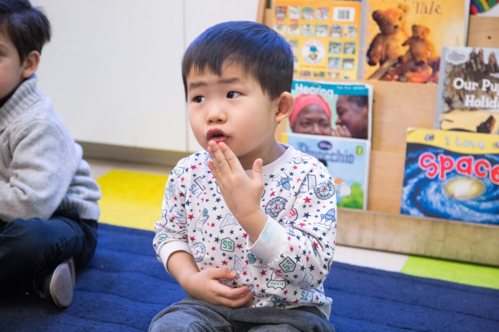A young child sits on a carpet in a classroom